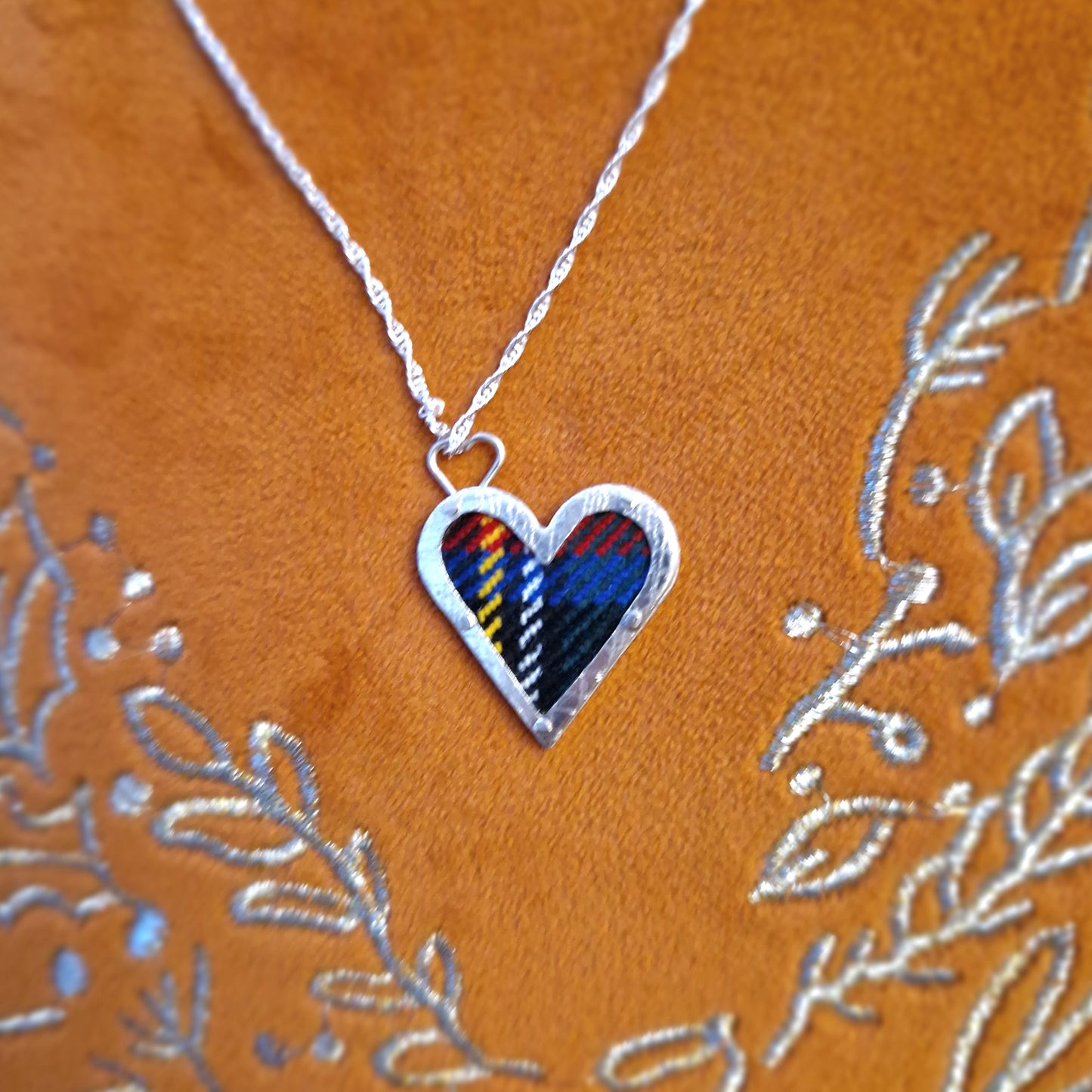 A hallmarked sterling silver heart pendant showcasing a fabric tartan inlay, held by silver wire rivets, suspended from an 18-inch silver rope chain.