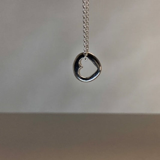 Close-up of a small, round solid sterling silver pendant with a central cut-out heart, approximately 1.2cm in diameter, suspended on an 18-inch silver chain.