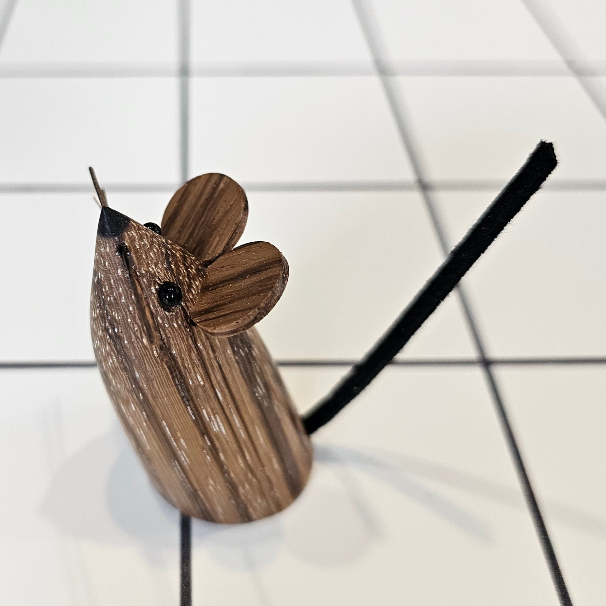 A decorative mouse, uniquely carved from local wood, standing upright with small eyes, ears, whiskers and a leather tail