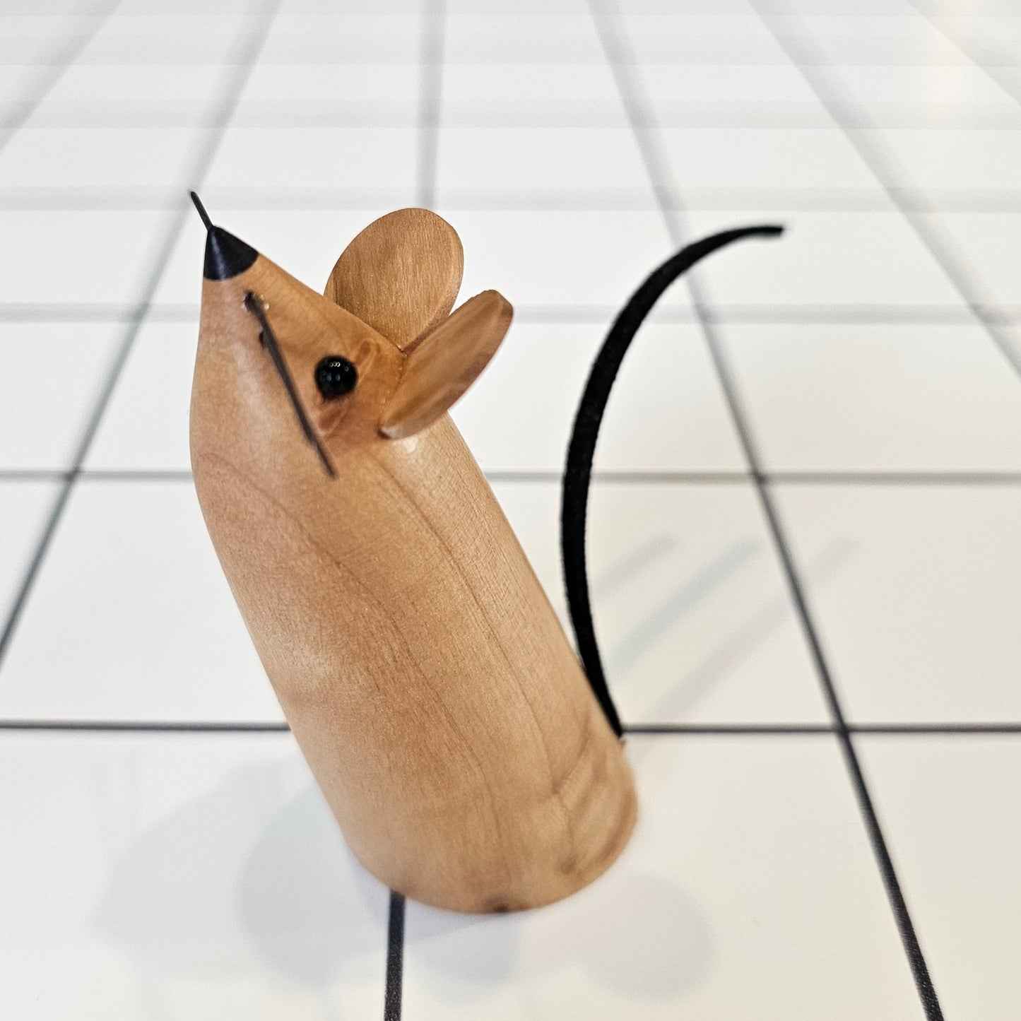 A decorative mouse, uniquely carved from local wood, standing upright with small eyes, ears, whiskers and a leather tail