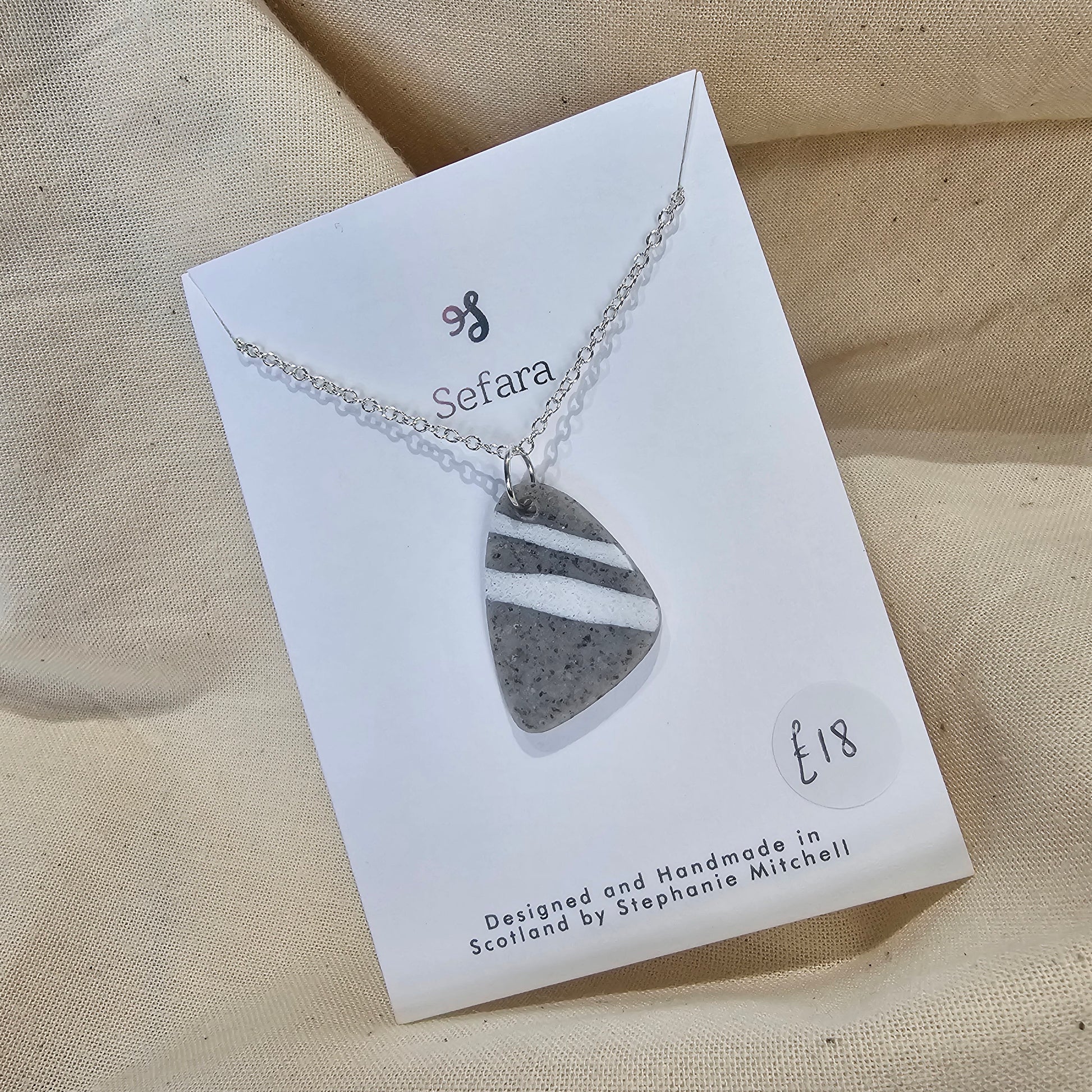 Handmade grey and white polymer clay pebble shaped pendant on 18-inch silver plated chain by Sefara Jewellery. Striped design.