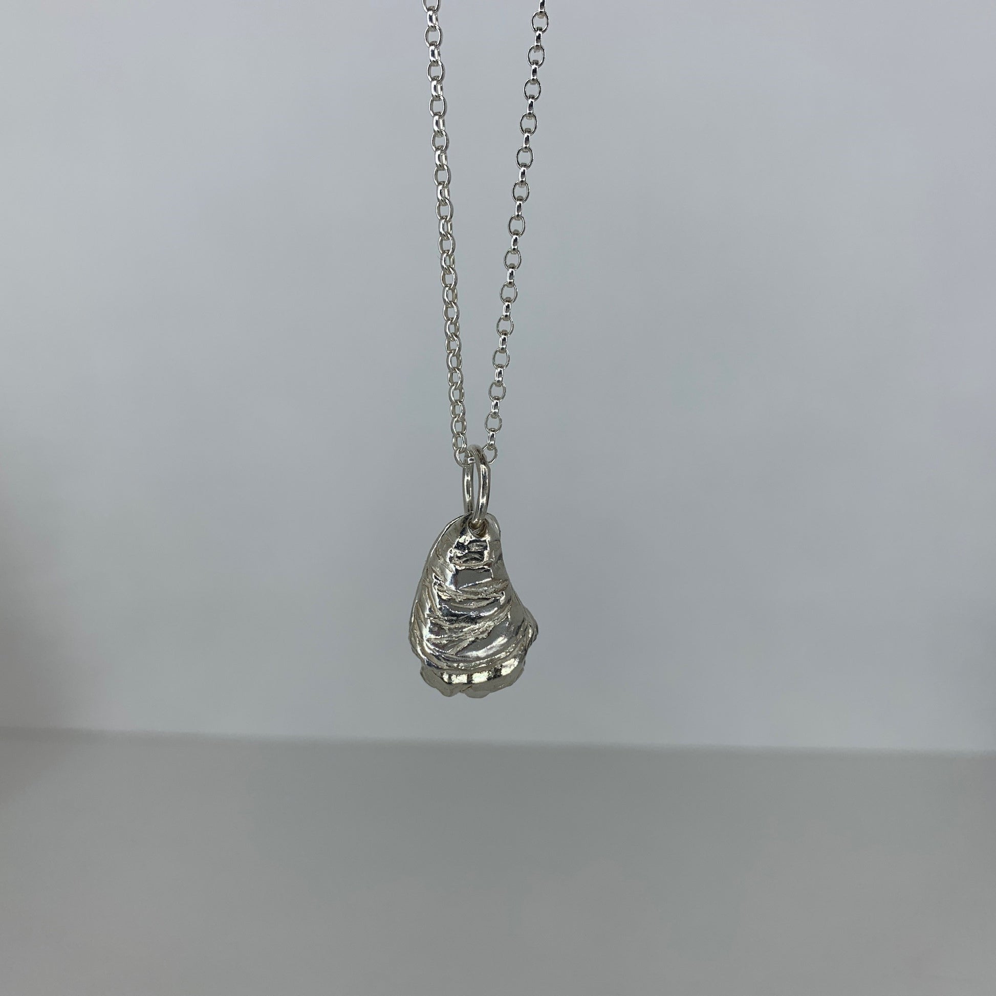 A silver oyster shell pendant on an 18-inch chain, displayed against a neutral background.