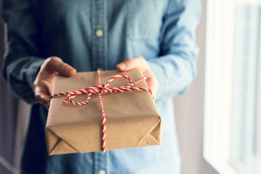 Person holding a brown paper gift box with red string, blurred background