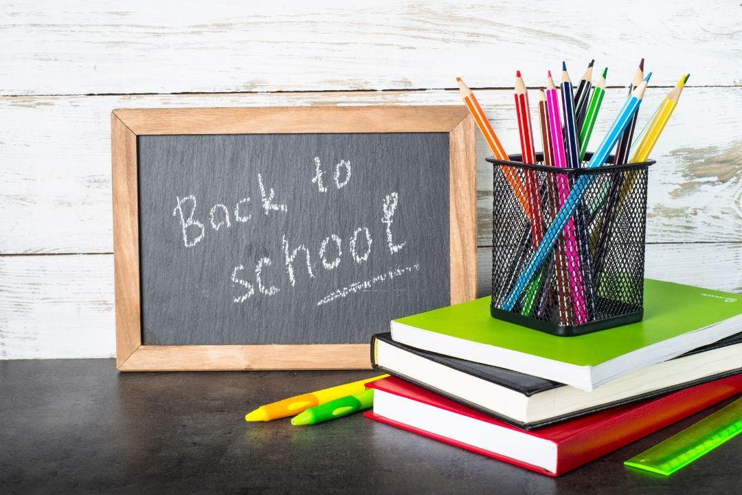 Back to school setup with chalkboard, books, and colorful pencils on a wooden surface.