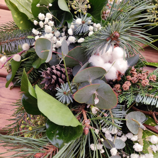 A close-up of fresh, green foliage and natural decorations onto a willow and moss wreath base during a workshop.