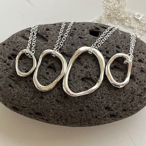 Four solid sterling silver pebble pendants of varying sizes (Small, Medium, Large, Extra Large) displayed on 18-inch silver chains.
