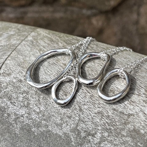 Four solid sterling silver pebble pendants of varying sizes (Small, Medium, Large, Extra Large) displayed on 18-inch silver chains.