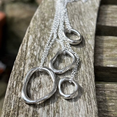 Four solid sterling silver pebble pendants of varying sizes (Small, Medium, Large, Extra Large) displayed on 18-inch silver chains.