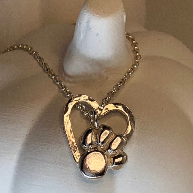 A silver pendant featuring a paw print inside a heart on a chain, displayed against a pumpkin