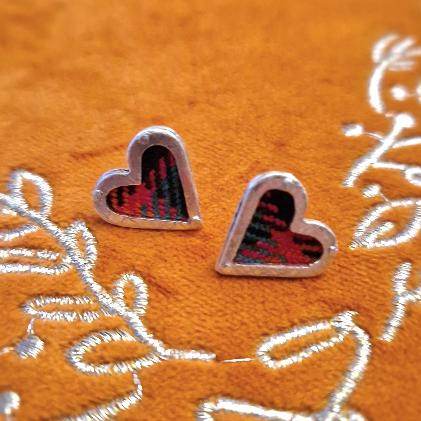 A pair of small, hallmarked sterling silver heart stud earrings featuring a tartan fabric inlay and secured with sterling silver pins and scrolls.