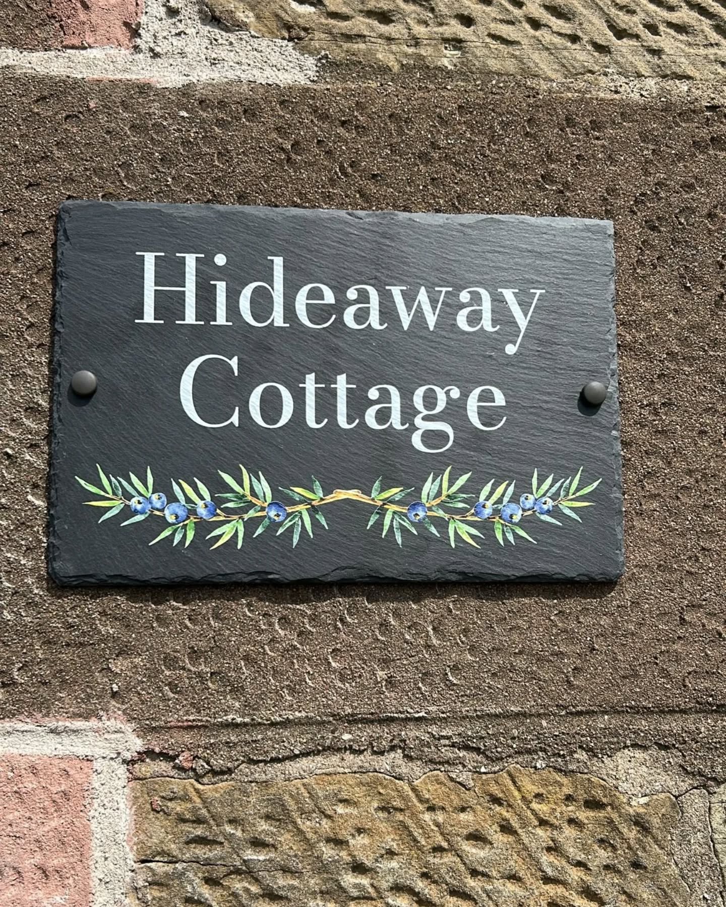 Slate house sign with 'Hideaway Cottage' on a brick wall