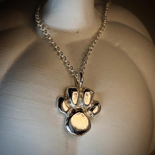 A solid silver pendant in the shape of a paw print, attached to an 18-inch chain, displayed on a pumpkin.