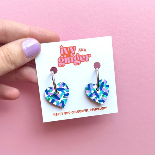 Hand painted white heart-shaped wooden hoop earrings with colourful confetti print, FSC wood, surgical steel lever back, 20mm, lightweight and gift-ready.
