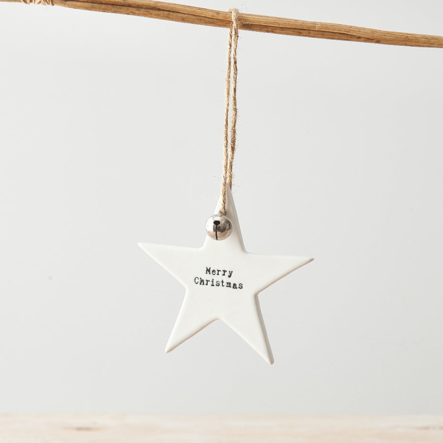 Chic white star-shaped ceramic Christmas decoration with a stamped "Merry Christmas" slogan, a small silver bell, and a jute string hanger.