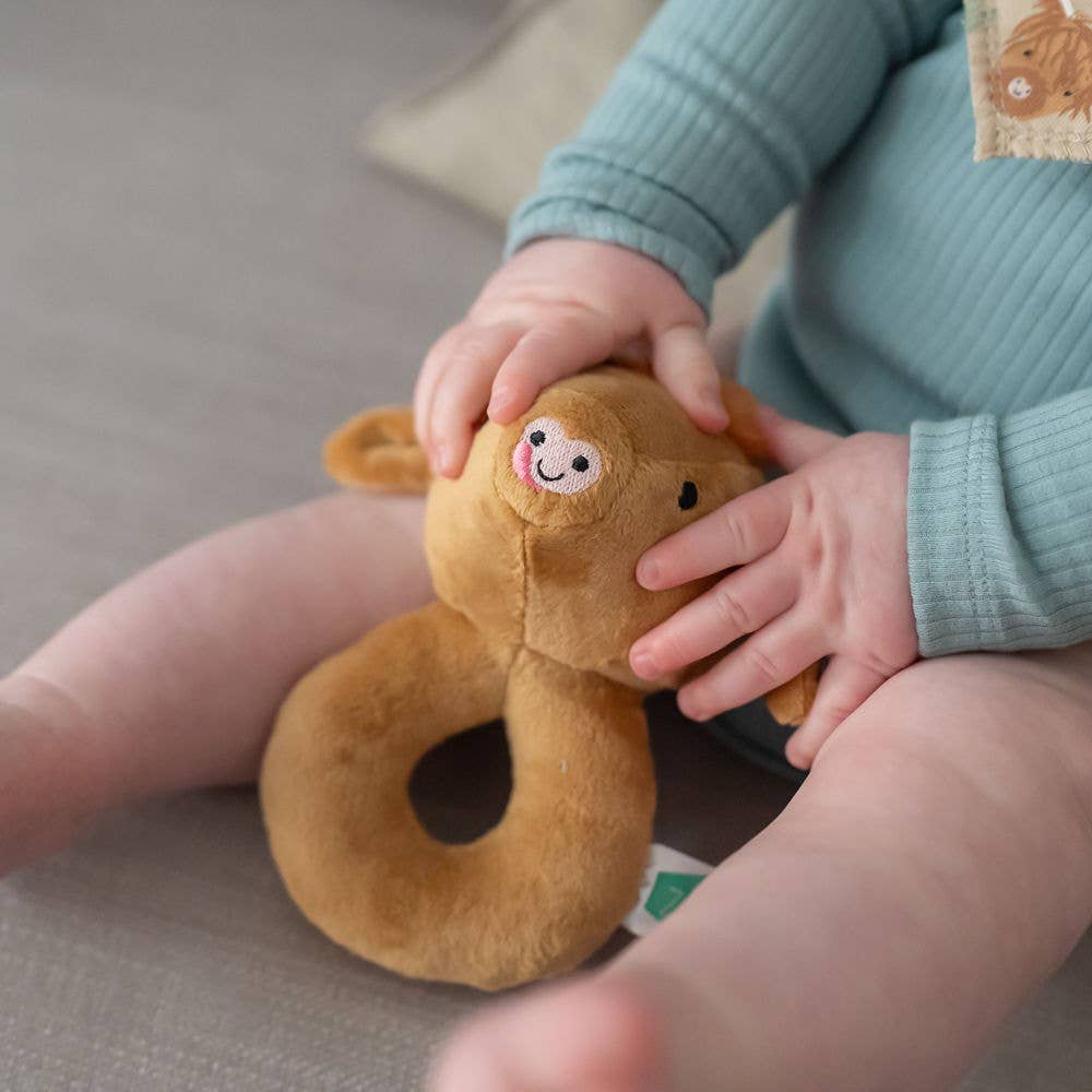 Child holding Soft Highland Cow plush baby rattle with gentle sensory sound, perfect for newborns