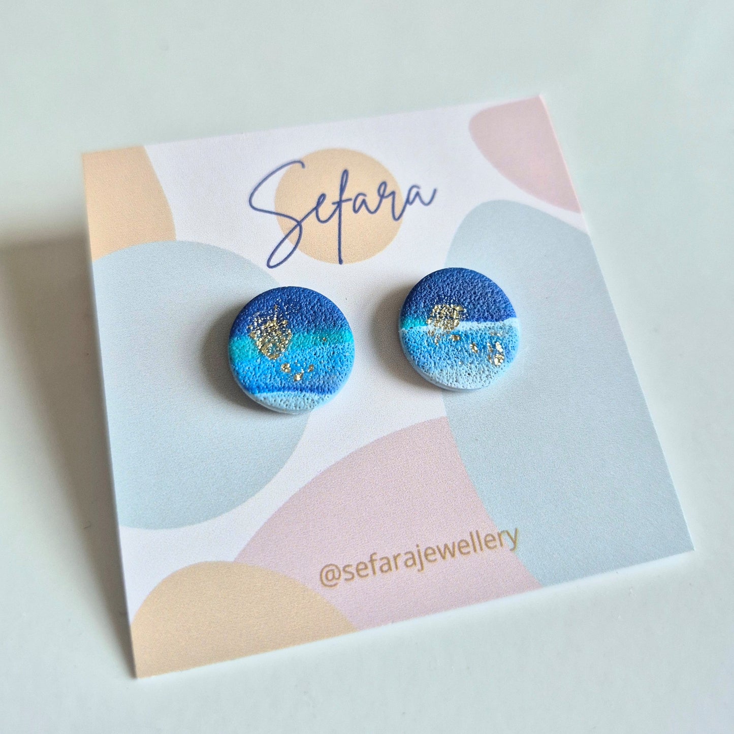 Blue and gold patterned earrings on a colourful card with 'Sefara' branding.