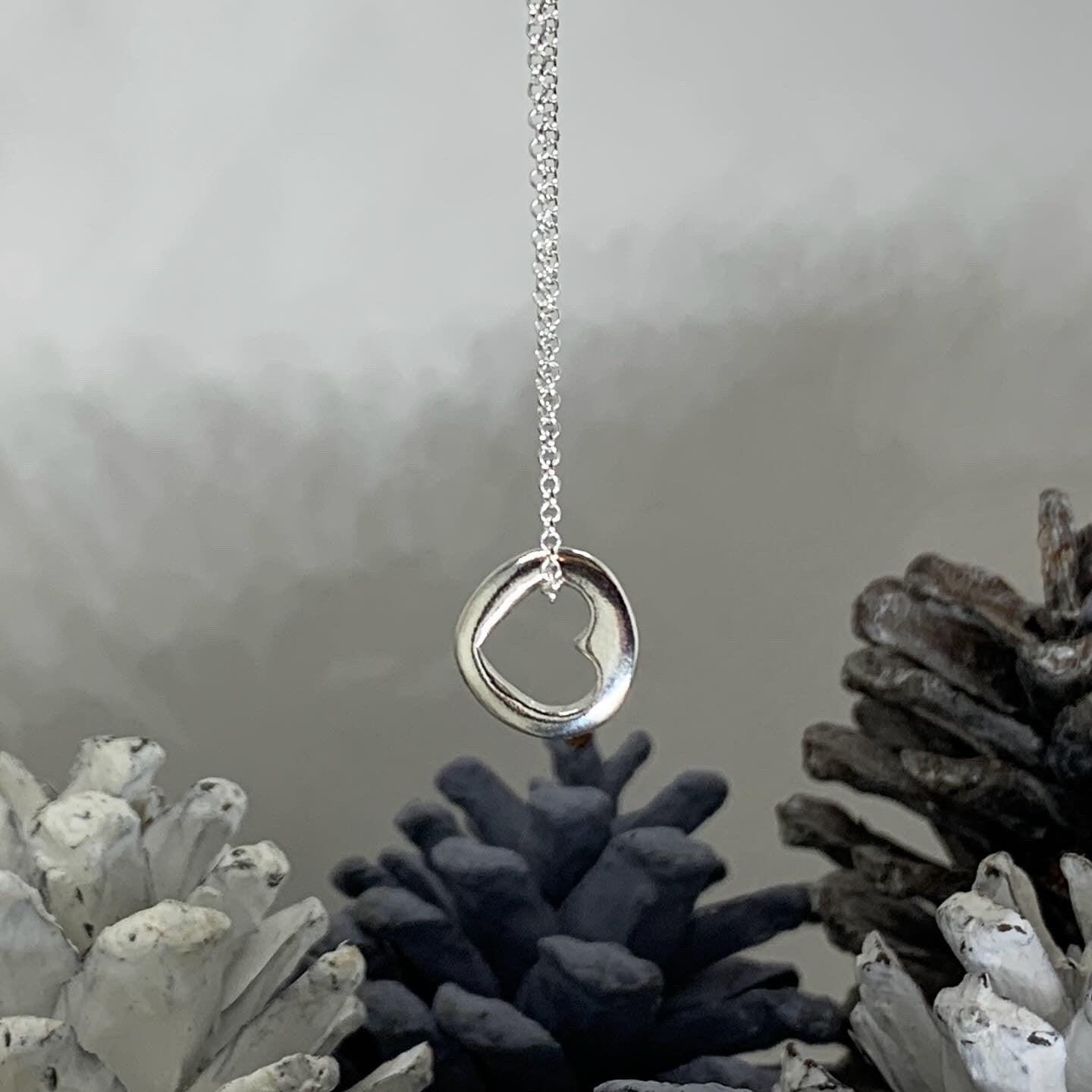 Close-up of a small, round solid sterling silver pendant with a central cut-out heart, approximately 1.2cm in diameter, suspended on an 18-inch silver chain.
