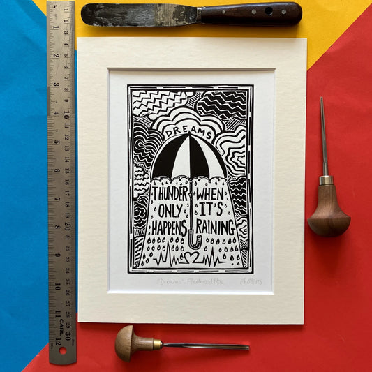 Black-and-white hand-printed linocut artwork titled “Dreams” by Pamela, inspired by Fleetwood Mac’s 1977 song, featuring bold carved textures, mounted in an antique white frame.