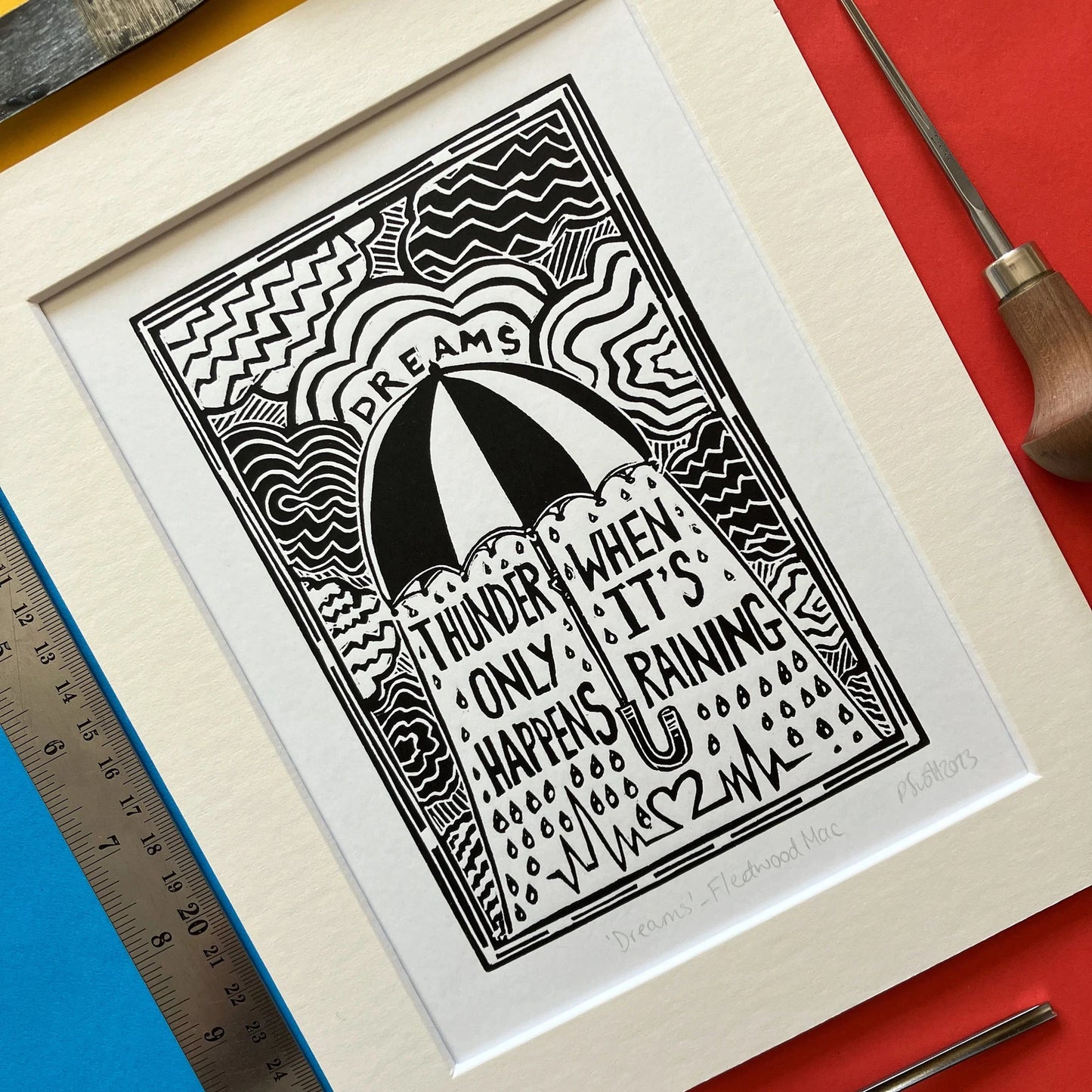 Black-and-white hand-printed linocut artwork titled “Dreams” by Pamela, inspired by Fleetwood Mac’s 1977 song, featuring bold carved textures, mounted in an antique white frame.