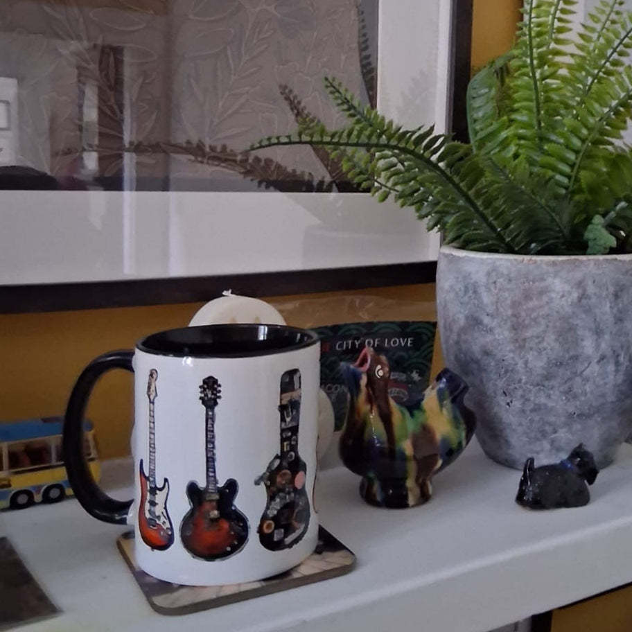 Mug with guitar design on a coaster, next to a plant and decorative items.