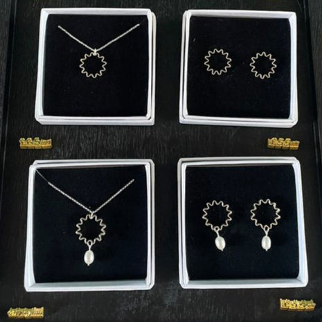Mini Ondulée pearl pendant necklace with small delicate drop pearl, shown gift boxed in matching jewellery sets. Necklaces and earrings displayed in black cases on a textured surface.