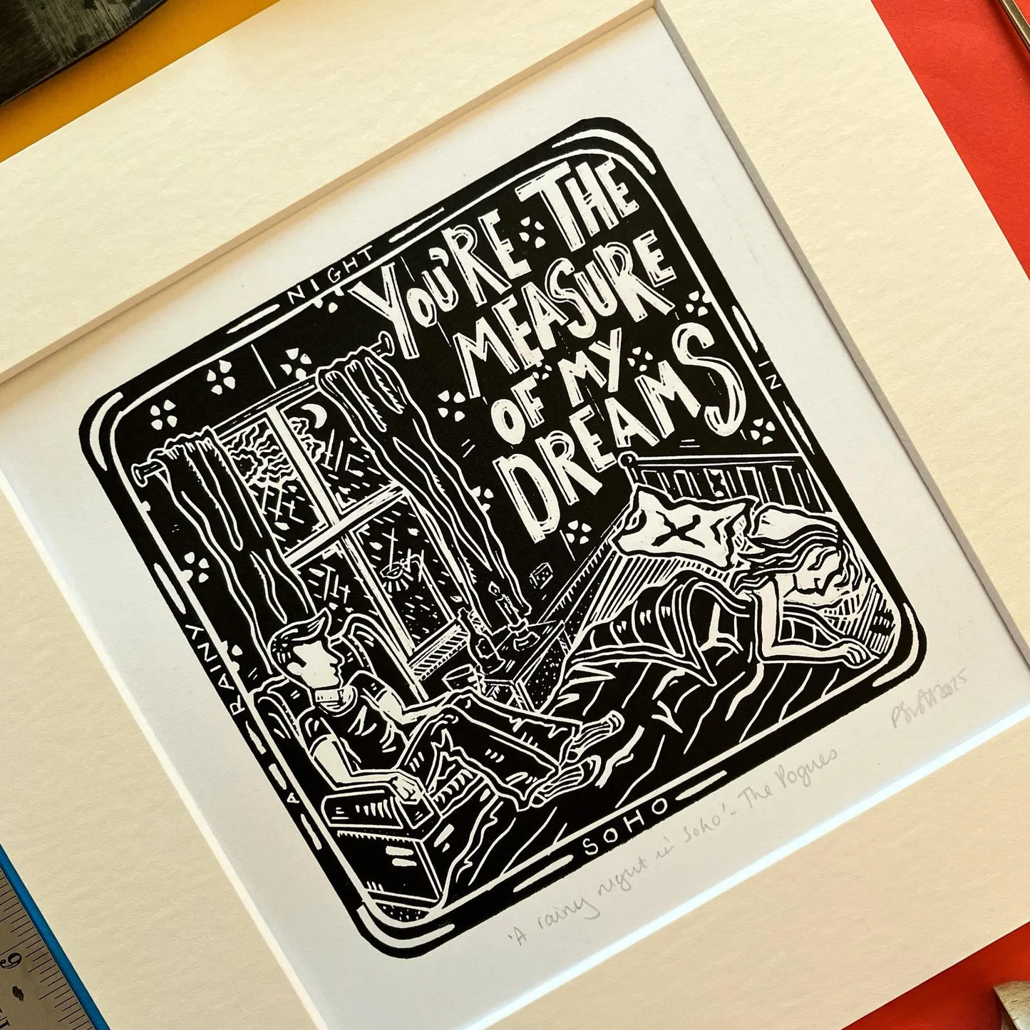 An original black and white linocut print featuring imagery inspired by The Pogues song 'A Rainy Night in Soho', mounted on antique white card.
