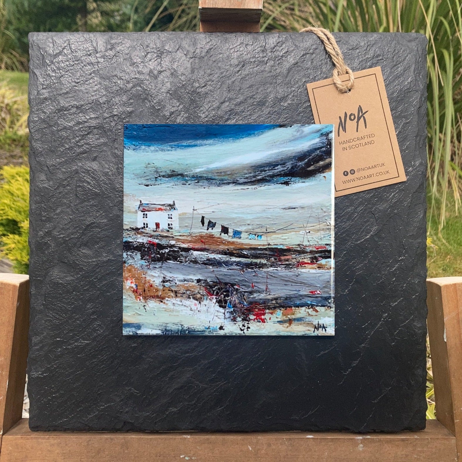 A ceramic tile print of a colourful painting titled 'Road to the Shee', showing a small house nestled in the Scottish Highlands, available mounted on natural slate or framed.