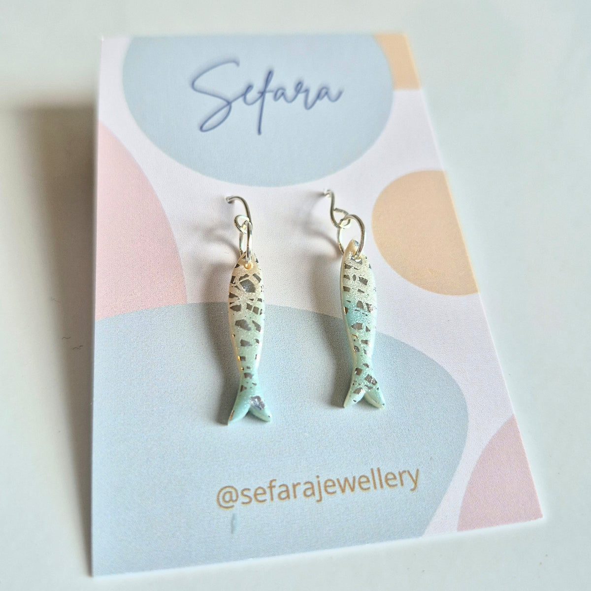 Sparkle fish-shaped earrings on a colourful card with 'Sefara' branding