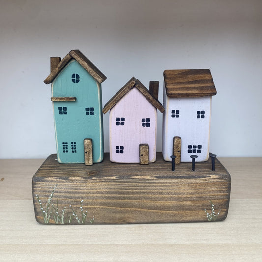 Handcrafted trio of wooden houses on block with rustic metal details in green, pink, and white