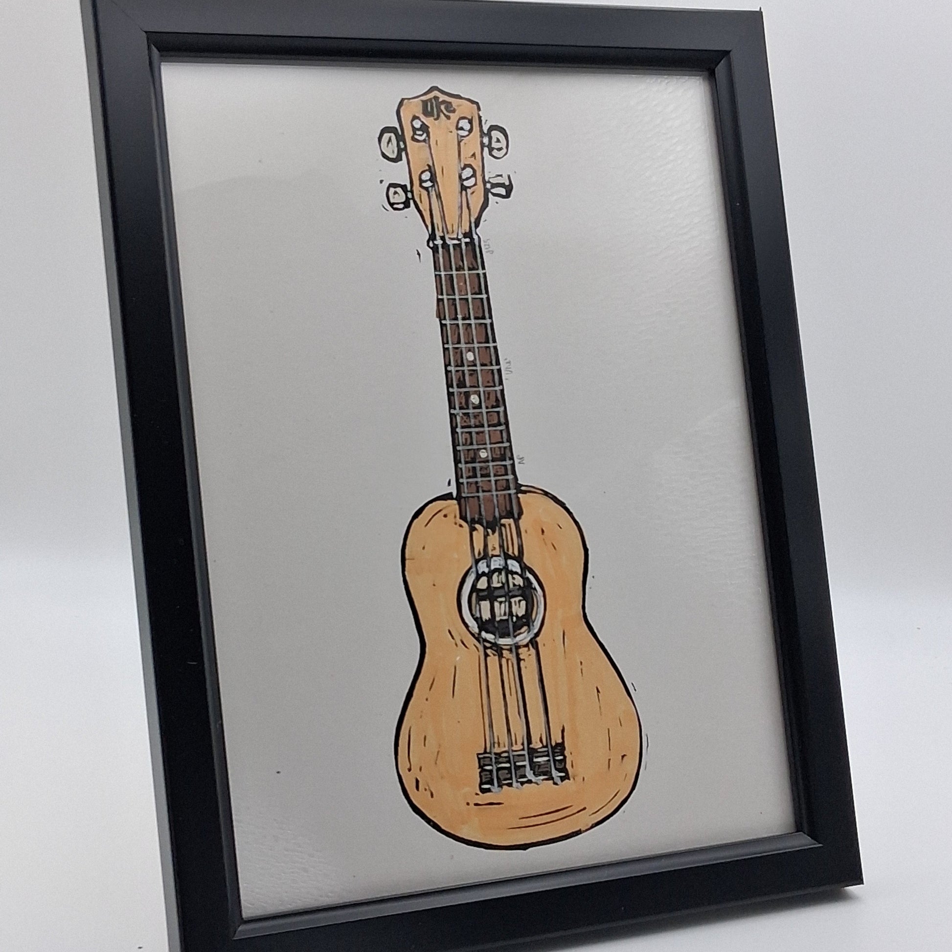A small, colourful linocut print illustrating a ukulele or uke, mounted in a small 7" x 9" black frame.
