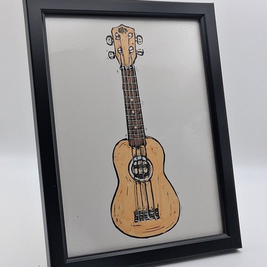 A small, colourful linocut print illustrating a ukulele or uke, mounted in a small 7" x 9" black frame.