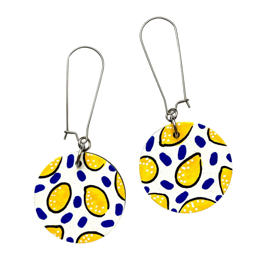 A pair of white lemon drop circle dangle earrings with silver hooks, featuring a pattern of yellow lemon-like shapes on a white background.