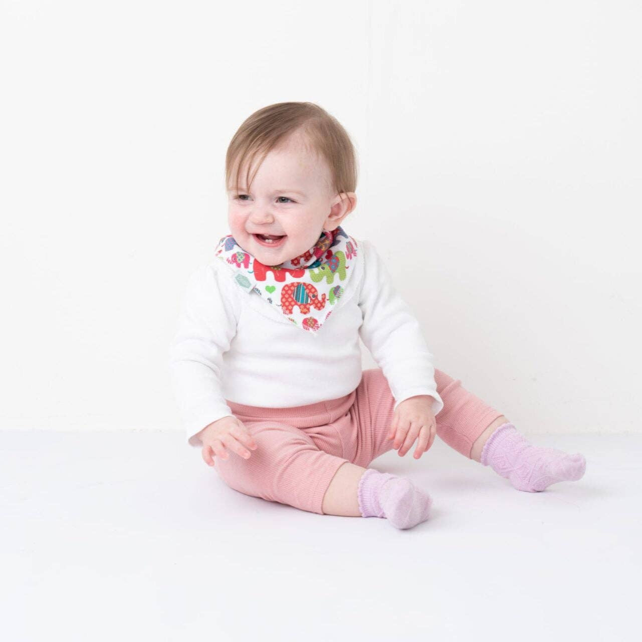 Baby sitting on a white background wearing Ethnic elephants print bandana bib for babies with soft cotton and fleece layers