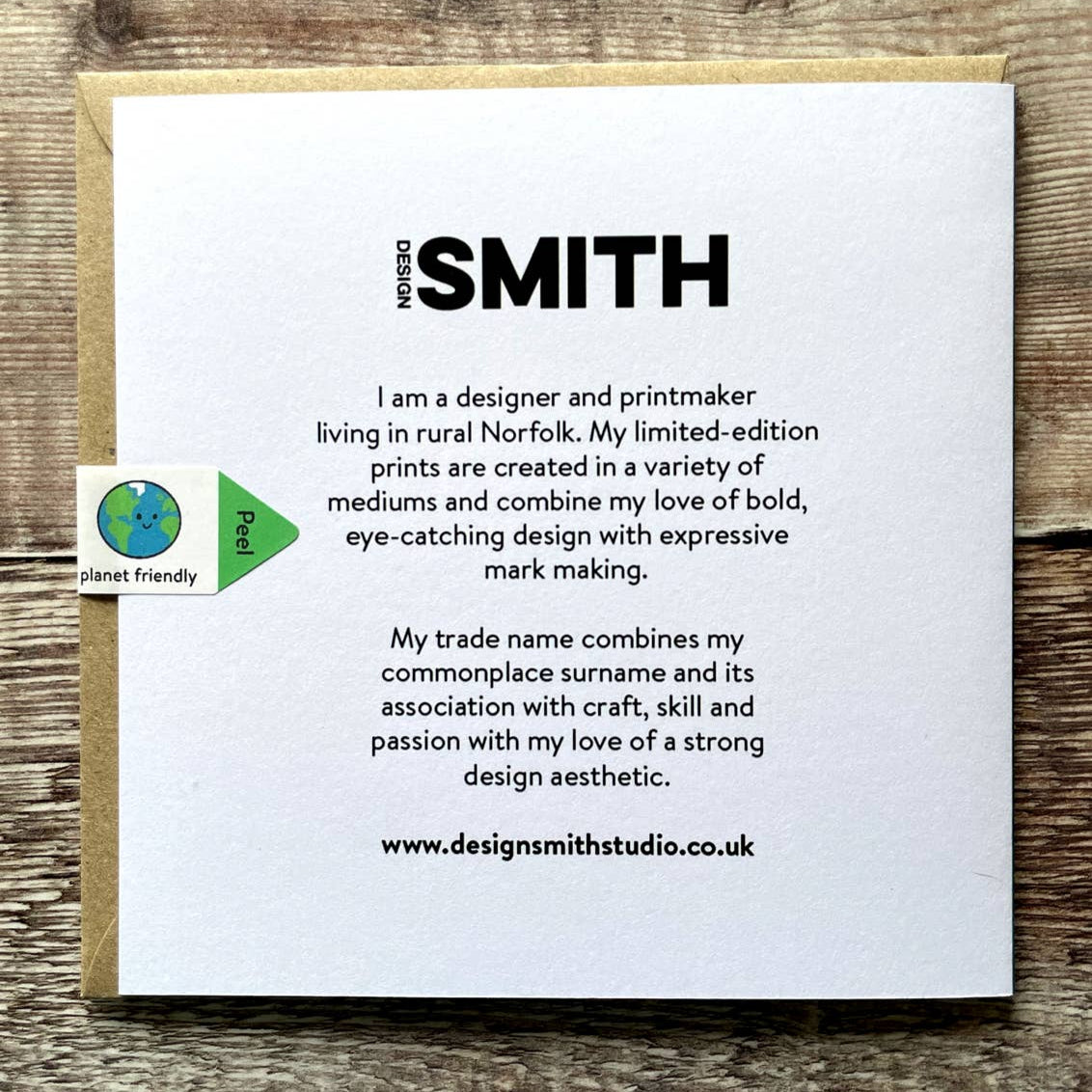 Back of white card with text about the designer and printmaker named Design Smith on a wooden surface