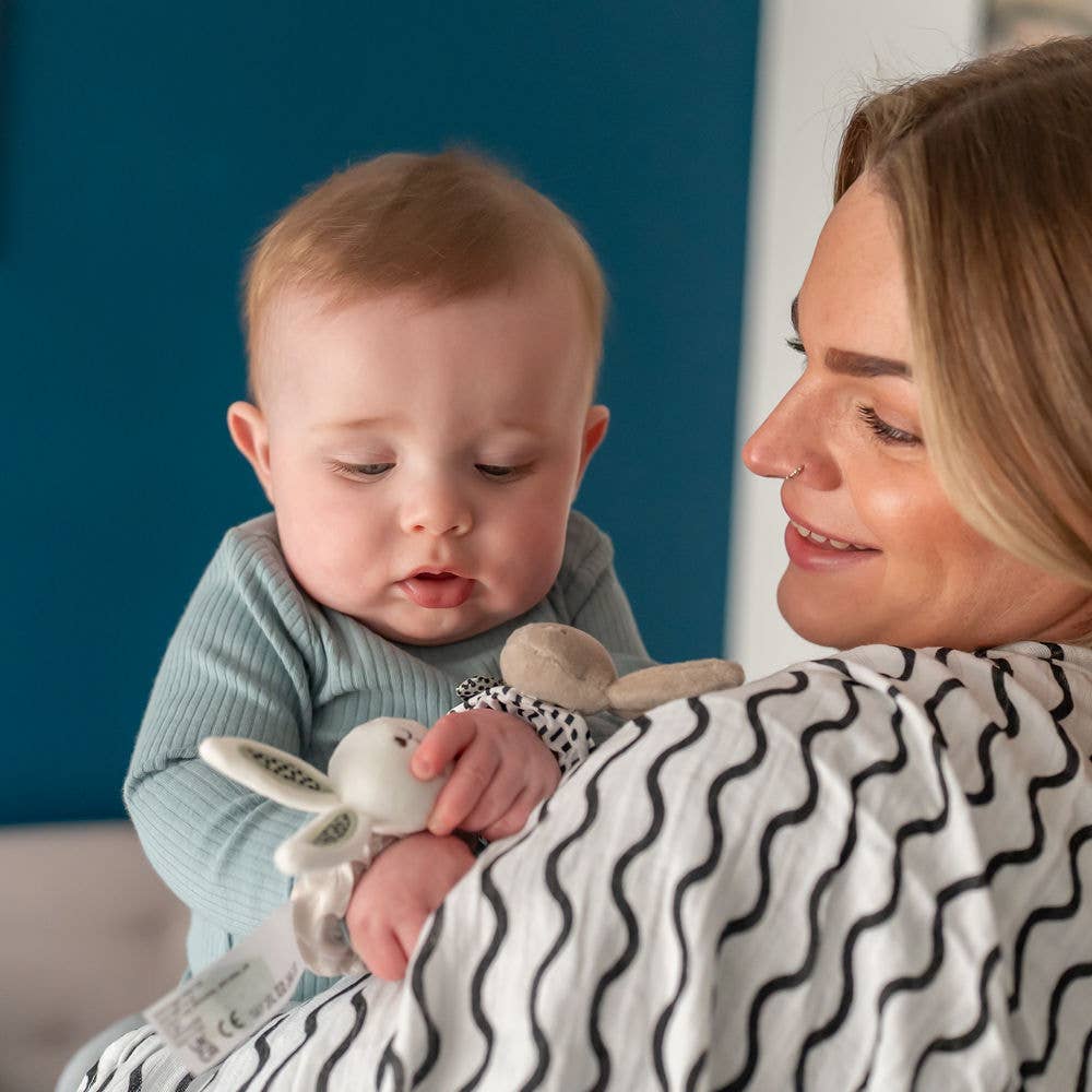 Woman holding a baby with black and white muslin draped over her shoulder