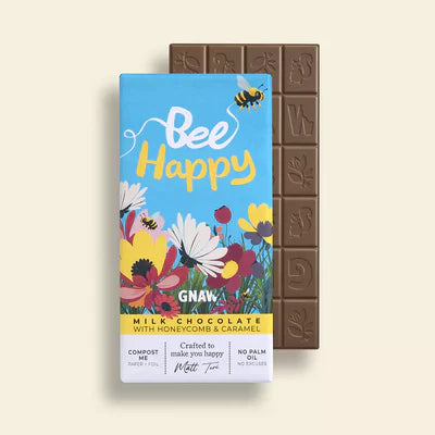A chocolate bar with 'BEE HAPPY' branding on the packaging, featuring floral designs and a chocolate bar with caramel chunks.