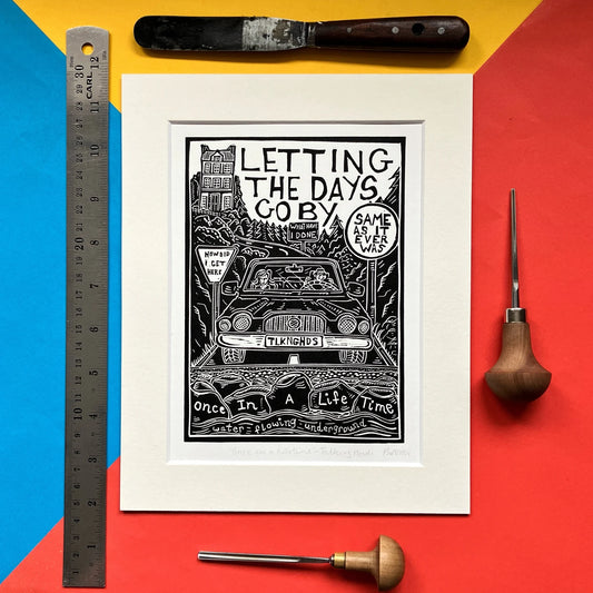 An original black and white linocut print featuring lyrics or imagery inspired by the Talking Heads song 'Once in a Lifetime', mounted on antique white card.