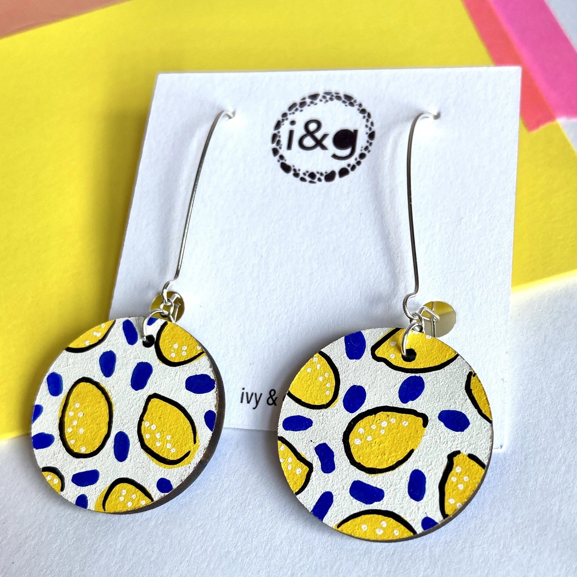 A pair of white lemon drop circle dangle earrings with silver hooks, featuring a pattern of yellow lemon-like shapes on a white background.