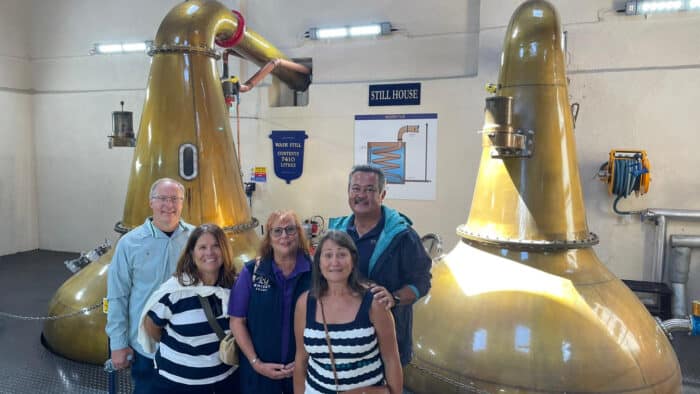 Group of people posing in front of large yellow stills in a distillery setting.