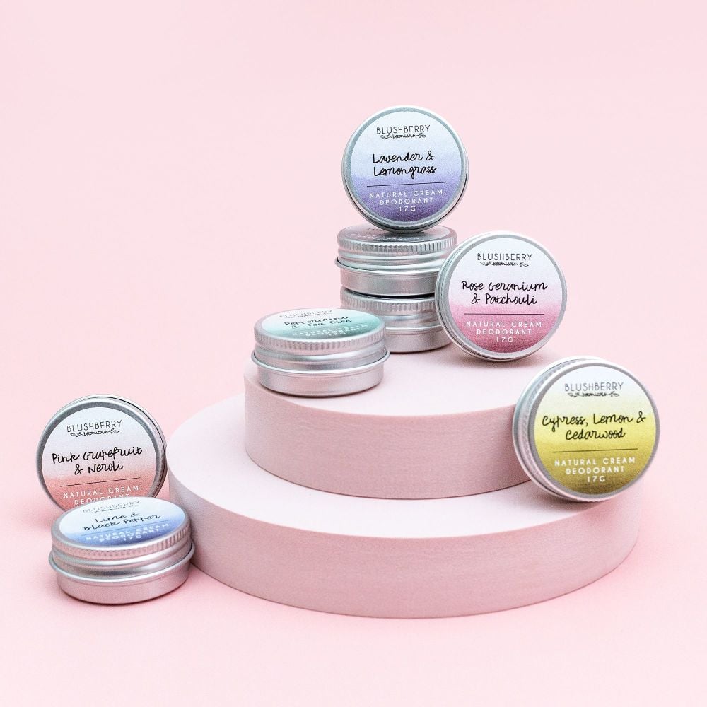 Collection of Blushberry natural cream deoderant tins on a pink platform with a light pink background