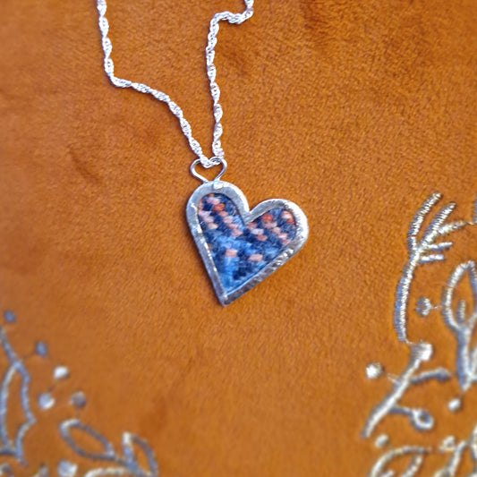 A hallmarked sterling silver heart pendant showcasing a fabric tartan inlay, held by silver wire rivets, suspended from an 18-inch silver rope chain.