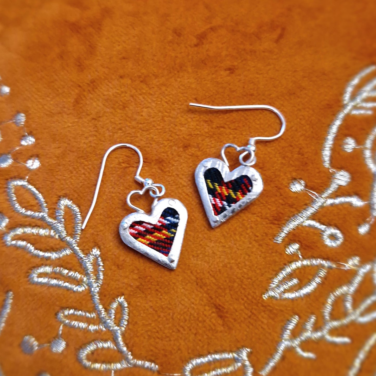 A pair of elegant hallmarked sterling silver heart-shaped drop earrings featuring a Royal Stewart tartan fabric inlay, suspended from sterling silver hooks.