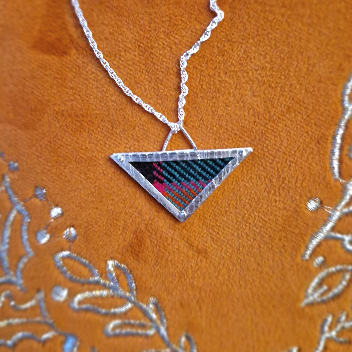 A hallmarked sterling silver triangle pendant showcasing a fabric tartan inlay, held by silver wire rivets, suspended from an 18-inch silver rope chain.