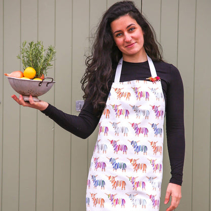 Woman wearing a Hairy Coo 100% cotton apron with bright Highland Cow print and holding a bowl of fruit against a wooden background