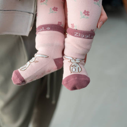 Baby's feet wearing pink cotton baby socks with bunny design, anti-slip soles and ribbed cuffs