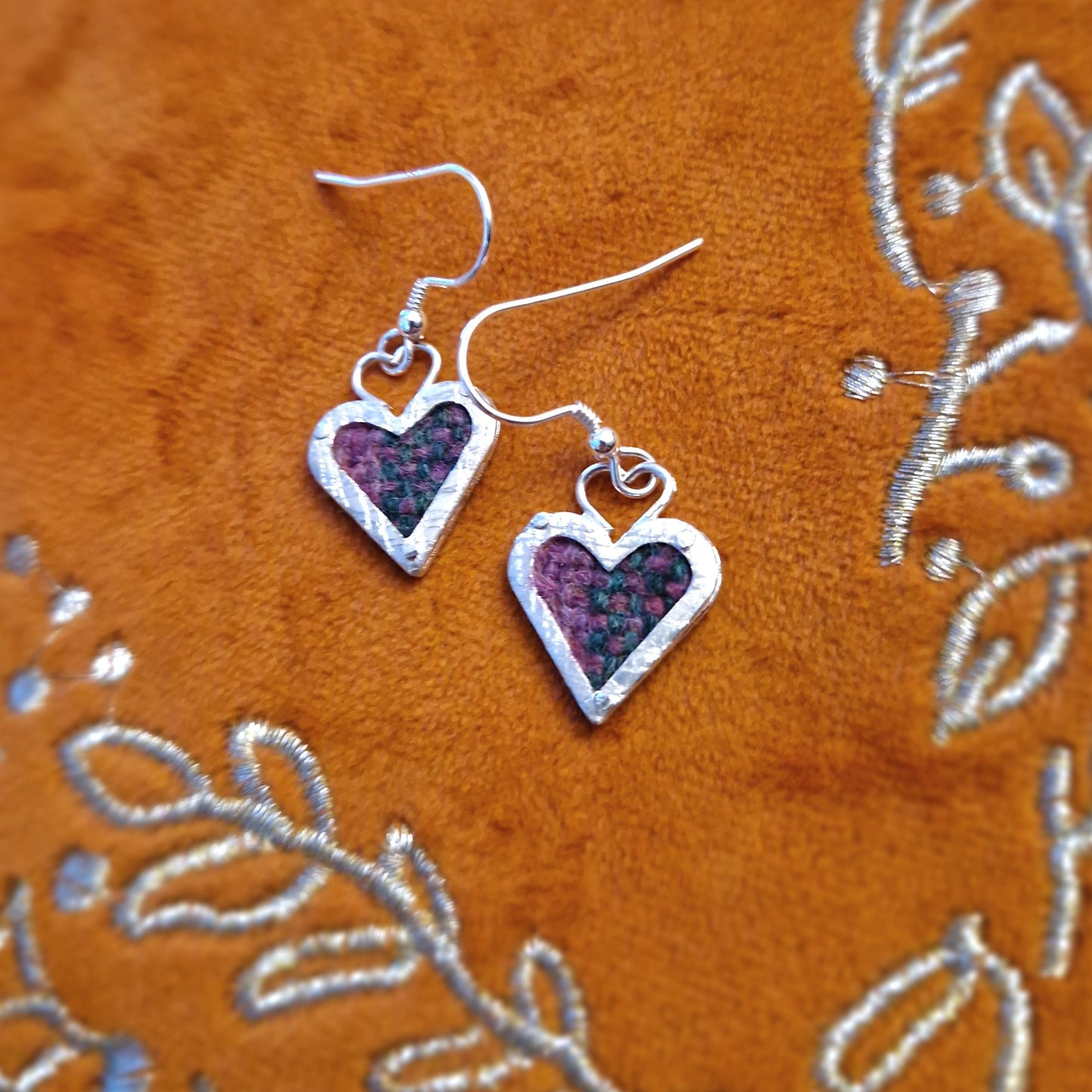 A pair of elegant hallmarked sterling silver heart-shaped drop earrings featuring a Discover Islay tartan fabric inlay, suspended from sterling silver hooks.