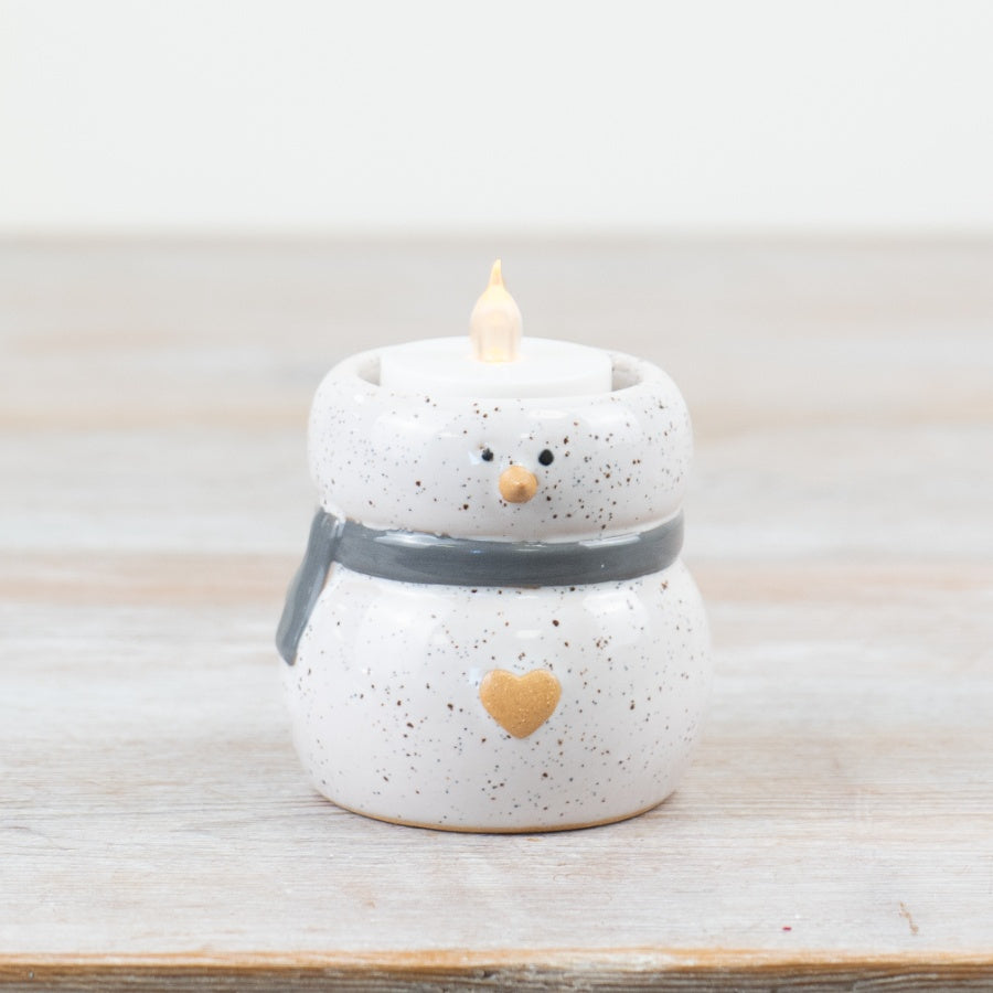 A small ceramic snowman tealight holder with a grey and white speckled finish, holding a candle.