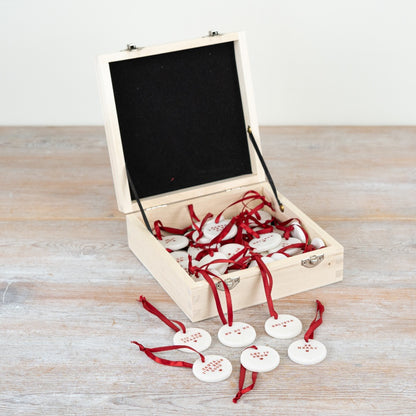 A set of six small round white ceramic Christmas pebble decorations with red text and a red ribbon. 