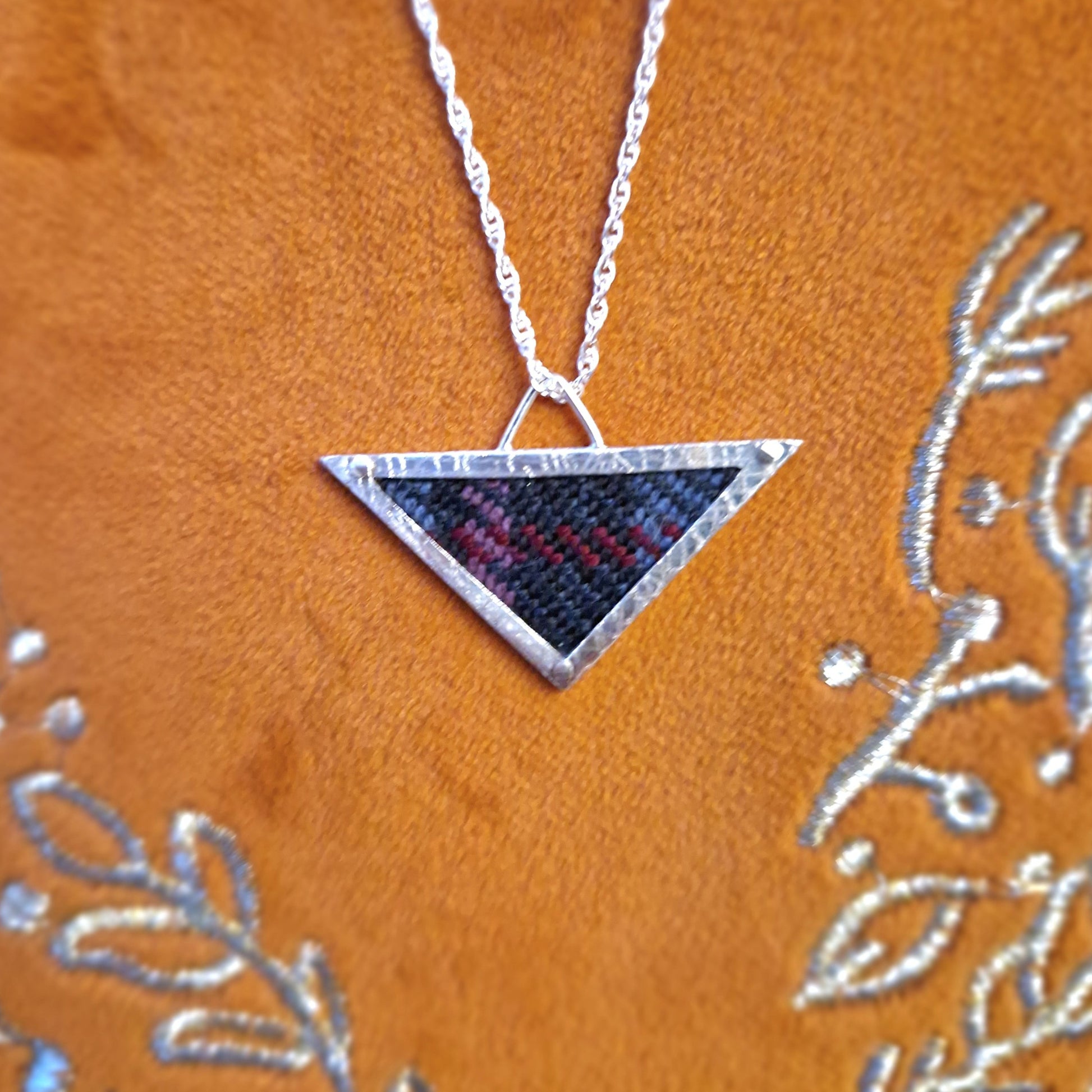 A hallmarked sterling silver triangle pendant showcasing a fabric tartan inlay, held by silver wire rivets, suspended from an 18-inch silver rope chain.