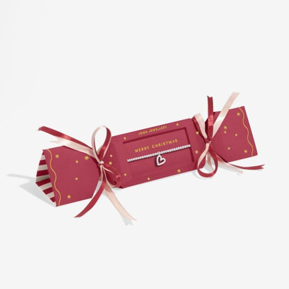 Red Joma Christmas cracker with silver-plated bracelet with heart shaped charm includes pink and red ribbons and MERRY CHRISTMAS text